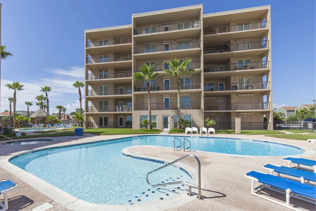 Een meerlaags hotel met een zwembad, terras en palmbomen.