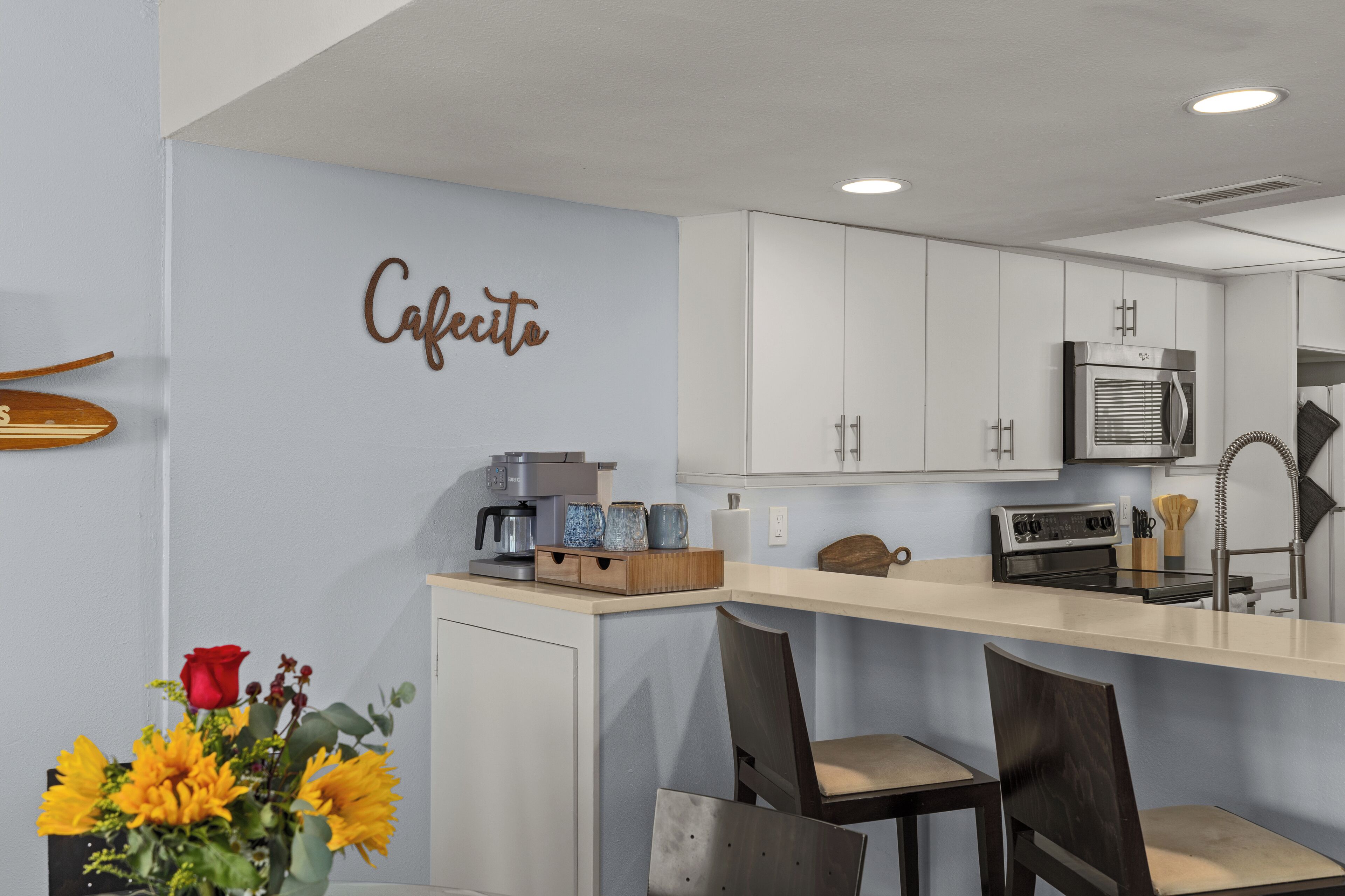 A modern kitchen with white cabinets, a coffee machine, and a countertop with a vase of sunflowers and a red rose.