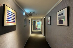 A hallway with framed artwork on the walls, a light switch, and a door at the end.