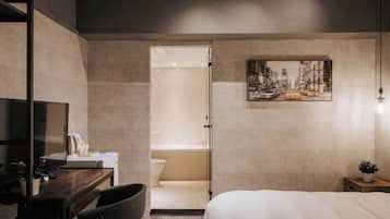A modern hotel room with a bed, desk, chair, and a painting on the wall.