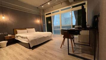 A modern bedroom with a bed, desk, and chair, large windows, and a view of the outdoors.