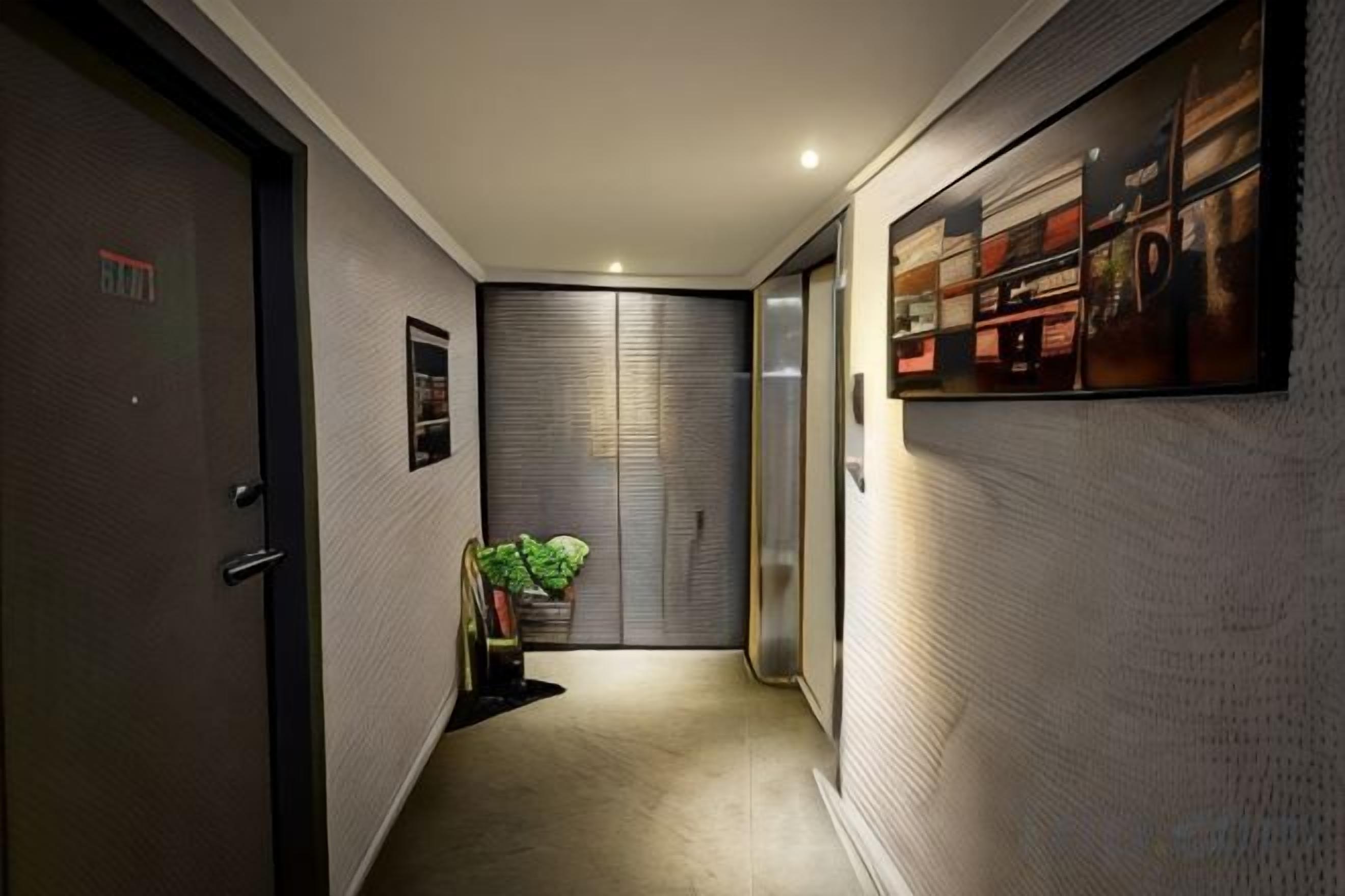 A hallway with a door, a plant, and a wall-mounted shelf with items.