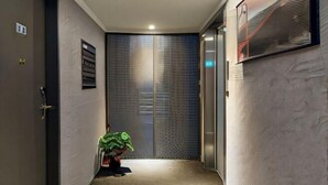 A hallway with a door, a plant, and a wall with a textured pattern. - Pure meworld hotel (Taipei)