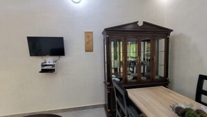 Un comedor con una mesa de madera, un televisor montado en la pared y un aparador con puertas de vidrio.