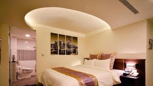 A hotel room with a bed, a bedside table with a lamp, a wall-mounted artwork, and a bathroom visible through an open door. - Good Hotel (Kaohsiung)