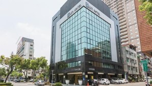 A modern hotel building with a glass facade, signage indicating it is the Sun Hotel, and a parking area in front. - Good Hotel (Kaohsiung)