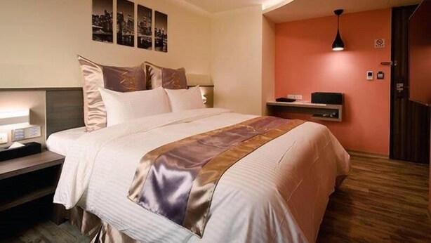 A hotel room with a bed, bedside table, wall art, and a desk lamp. - Good Hotel (Kaohsiung)