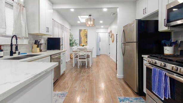A modern kitchen with white cabinets, a stainless steel refrigerator, a stove, and a dining area with a table and chairs. - Central 3-bedroom House with a Yard and Free Parking, Near Downtown (San Diego)