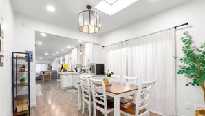 A modern kitchen with white cabinets, a dining area with white chairs, and a wooden floor. - Central 3-bedroom House with a Yard and Free Parking, Near Downtown (San Diego)