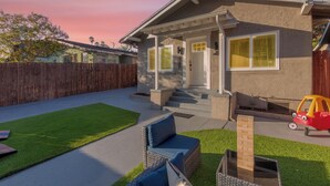 A residential house with a front porch, a small front yard with artificial grass, a wooden fence, and a red toy car. - Central 3-bedroom House with a Yard and Free Parking, Near Downtown (San Diego)