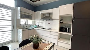 A modern kitchen with white cabinetry, a dining table with a vase, and a view through a sliding door. - Senshe B&B (Taitung)
