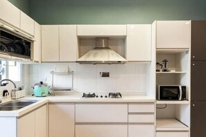 A modern kitchen with white cabinets, a gas stove, a microwave, and a dish rack. - Senshe B&B (Taitung)