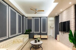 Un salon moderne avec un canapé, une table basse ronde, un ventilateur de plafond et un téléviseur fixé à un mur en briques.