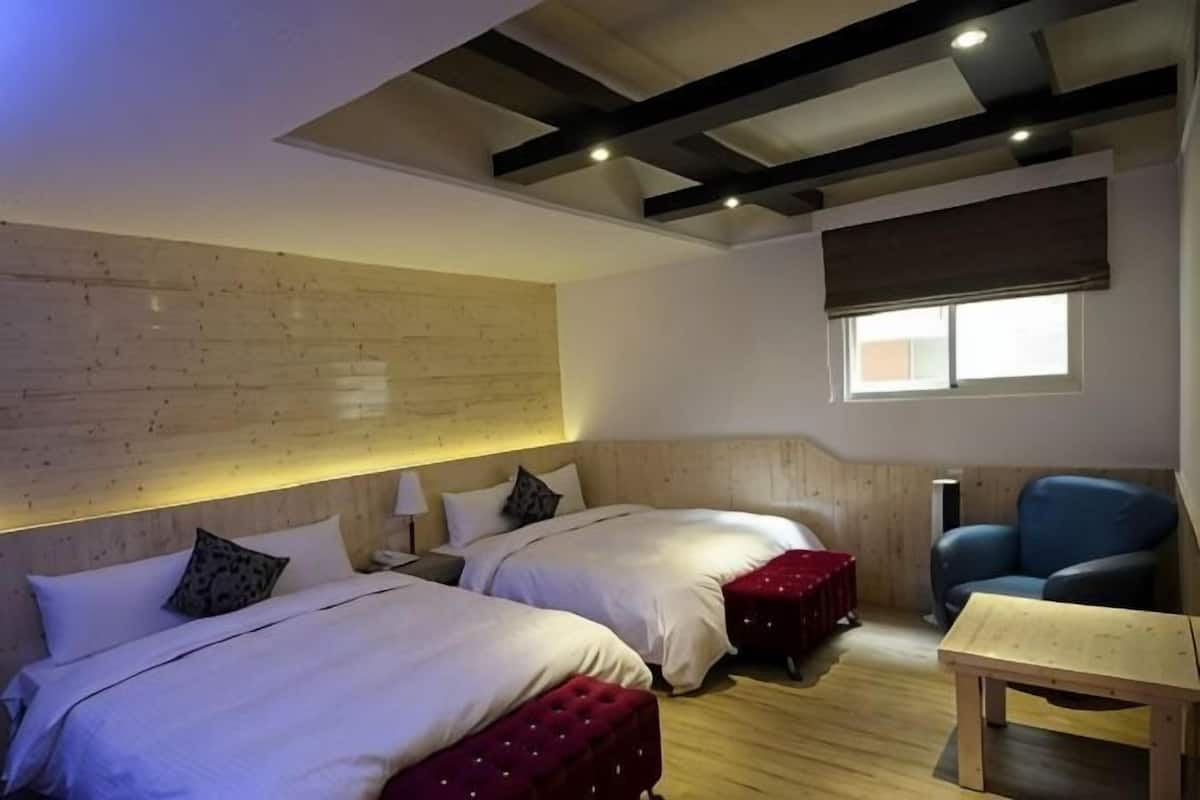 A room with two beds, a wooden ceiling, a window, and a chair.