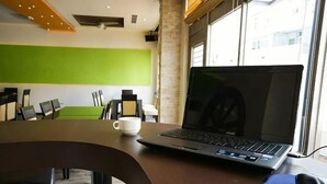 A laptop on a wooden table in a room with a green wall, a window, and a brick wall. - Penghu Royal Hotel (Penghu)
