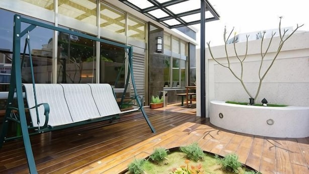A modern outdoor area with a swing set, a planter with trees, and a wooden deck. - Penghu Royal Hotel (Penghu)