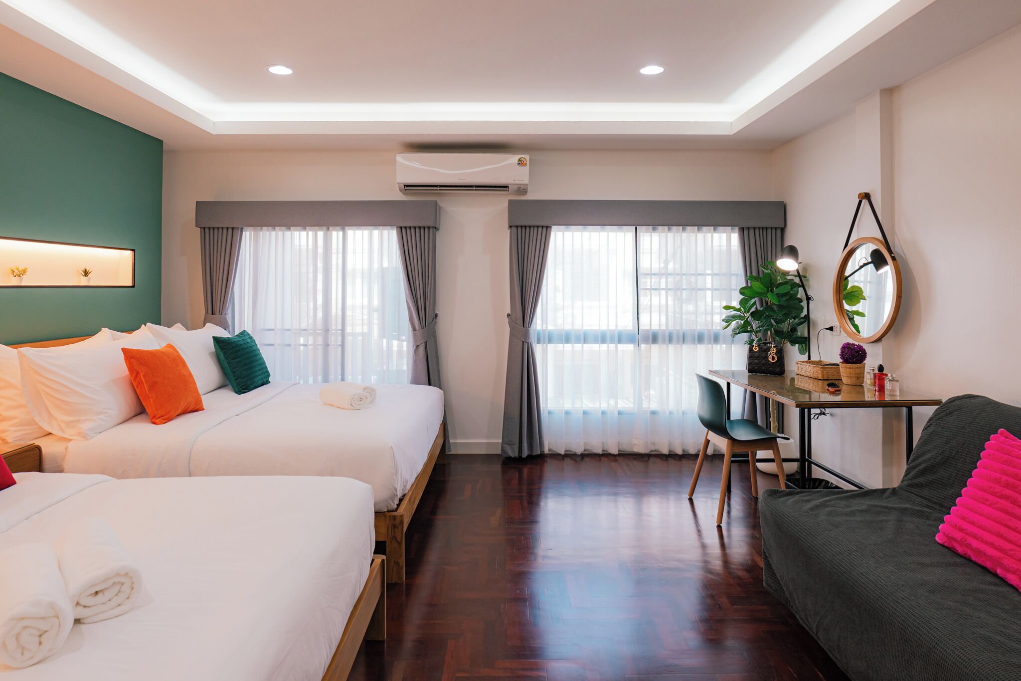 A hotel room with two beds, a desk, a chair, a potted plant, and a mirror.