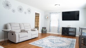 A modern living room with a beige sofa, a blue patterned rug, wooden flooring, a flat-screen TV, and decorative wall art. - Bright & Comfortable 3-bedroom Retreat in Cottondale. Only 6 miles from Campus! (Cottondale)