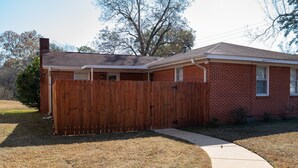 A single-story brick house with a wooden fence, a visible chimney, and a paved driveway. - Bright & Comfortable 3-bedroom Retreat in Cottondale. Only 6 miles from Campus! (Cottondale)