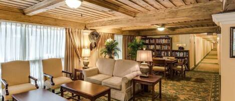 A room with a wooden ceiling, a sofa, a coffee table, a bookshelf, and a carpet with a leaf pattern.