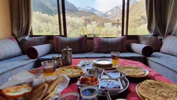 Un coin repas avec une table mise pour le repas, une vue sur les montagnes à travers de grandes fenêtres et un canapé avec des coussins.