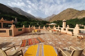 An outdoor terrace with seating and a view of mountains. - Dar Assarou - Toubkal National Park Lodge (Imlil)