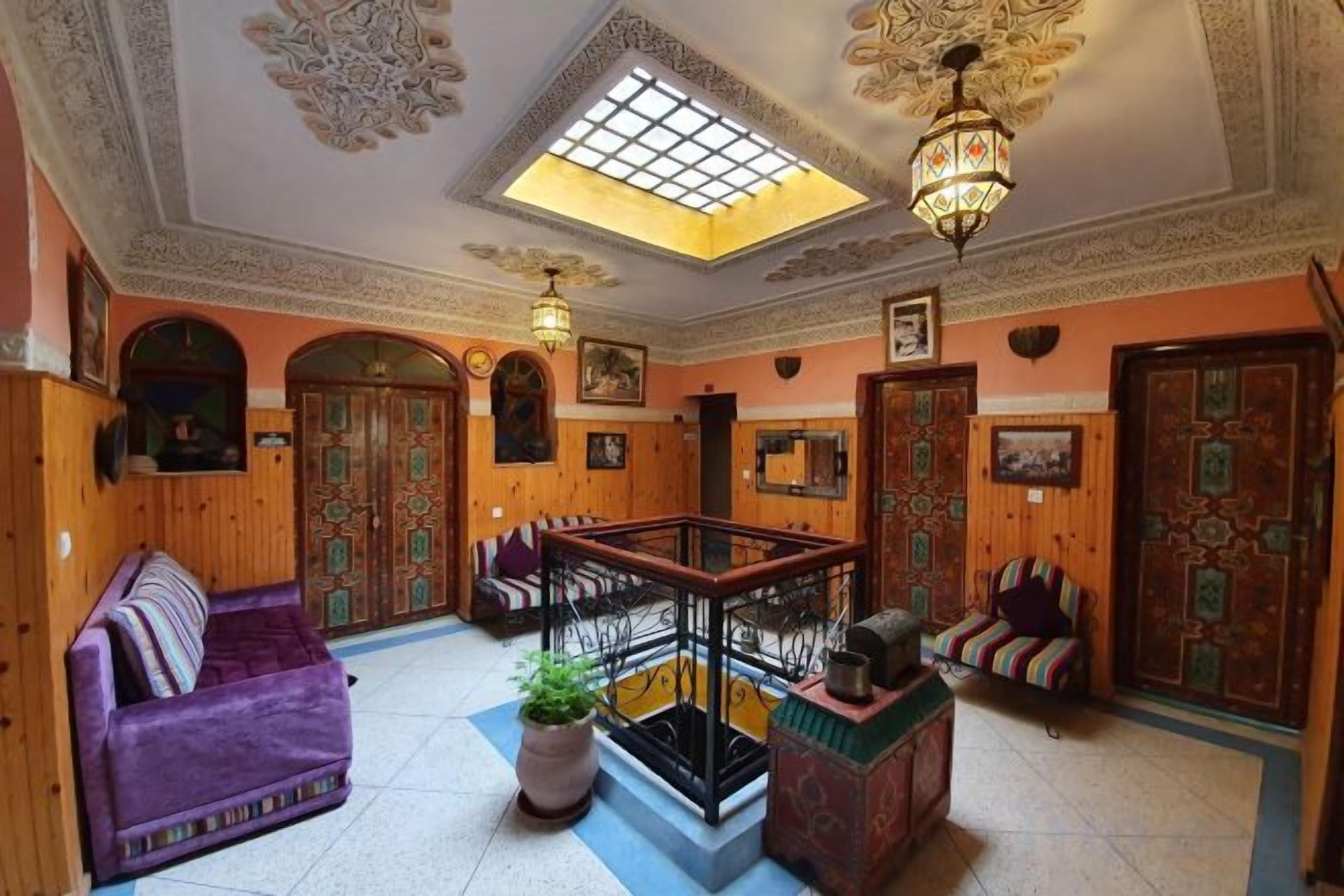 A traditional interior with a wooden floor, a central seating area with a sofa and chairs, a staircase, and a decorative ceiling.