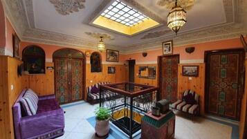 A traditional interior with a wooden floor, a central seating area with a sofa and chairs, a staircase, and a decorative ceiling.