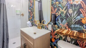 Une salle de bain avec un lavabo blanc, un robinet doré et un miroir orné d’un papier peint à motifs floraux.