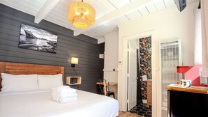 Une chambre d’hôtel avec un grand lit, une tête de lit en bois, un téléviseur fixé au mur et une porte donnant sur une salle de bain.