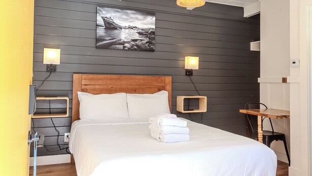 Een net opgemaakt bed met witte lakens, een houten hoofdbord en een aan de muur hangend schilderij van een rotsachtig landschap.