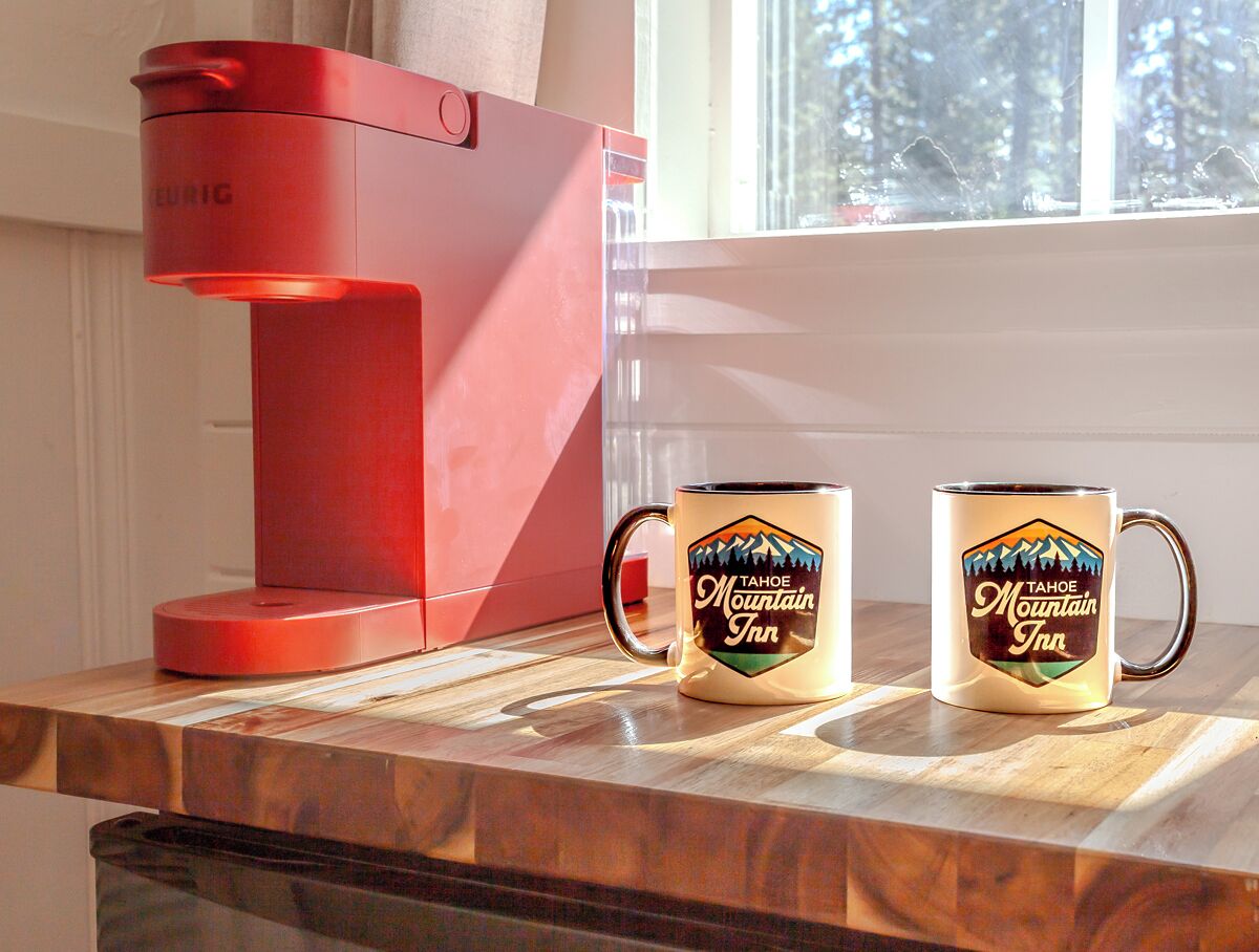 Una cafetera roja y dos tazas con el logotipo de 'Tahoe Mountain Inn' sobre una encimera de cocina.