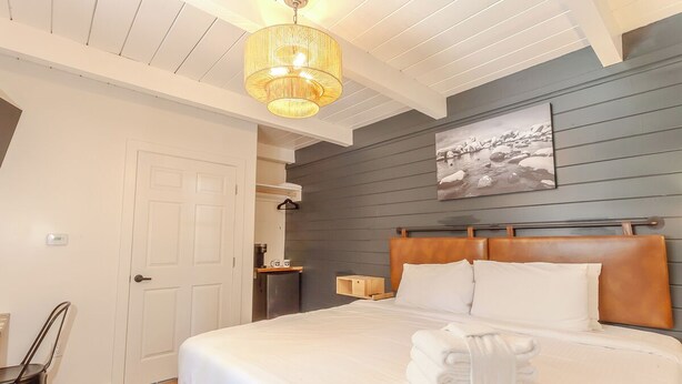 Een keurig opgemaakt slaapkamer met een groot bed, een houten hoofdbord, een hanglamp, een schilderij aan de muur en een klein houten nachtkastje.