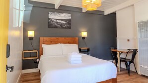Een slaapkamer met een houten hoofdeinde, een bed met witte lakens, twee nachtkastjes, een bureau met stoel, en een kroonluchter.