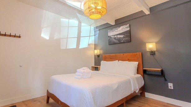 Een net opgemaakt bed met witte lakens, een houten hoofdbord en een nachtkastje met een lamp.