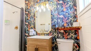 Een badkamer met bloemenbehang, een witte wastafel, een spiegel met verlichting en een toilet.
