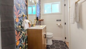 Een badkamer met bloemenbehang, een gouden wastafel, een wit toilet en een raam.