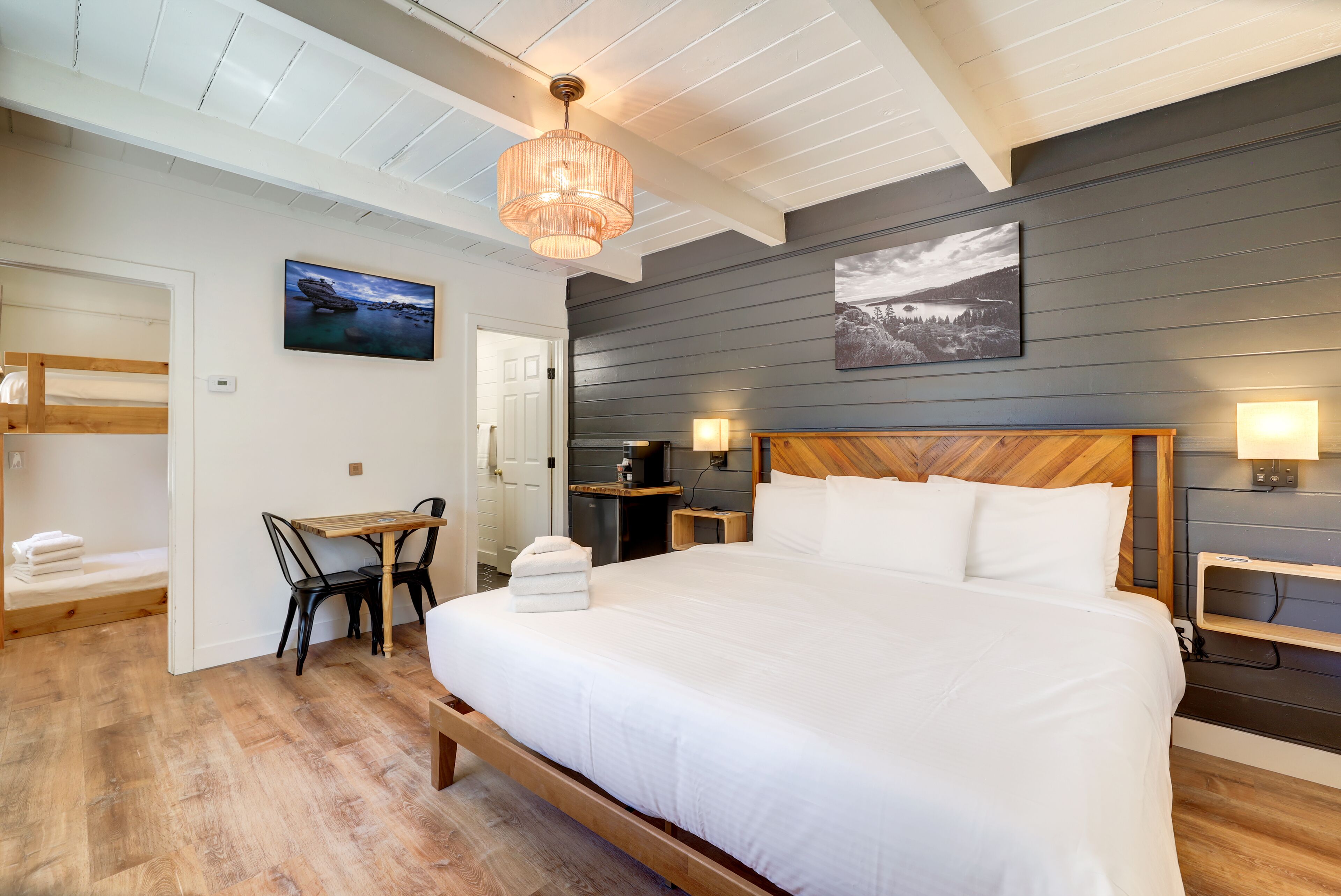 A bedroom with a large bed, wooden headboard, two bedside tables with lamps, a small desk with a chair, and a painting on the wall.