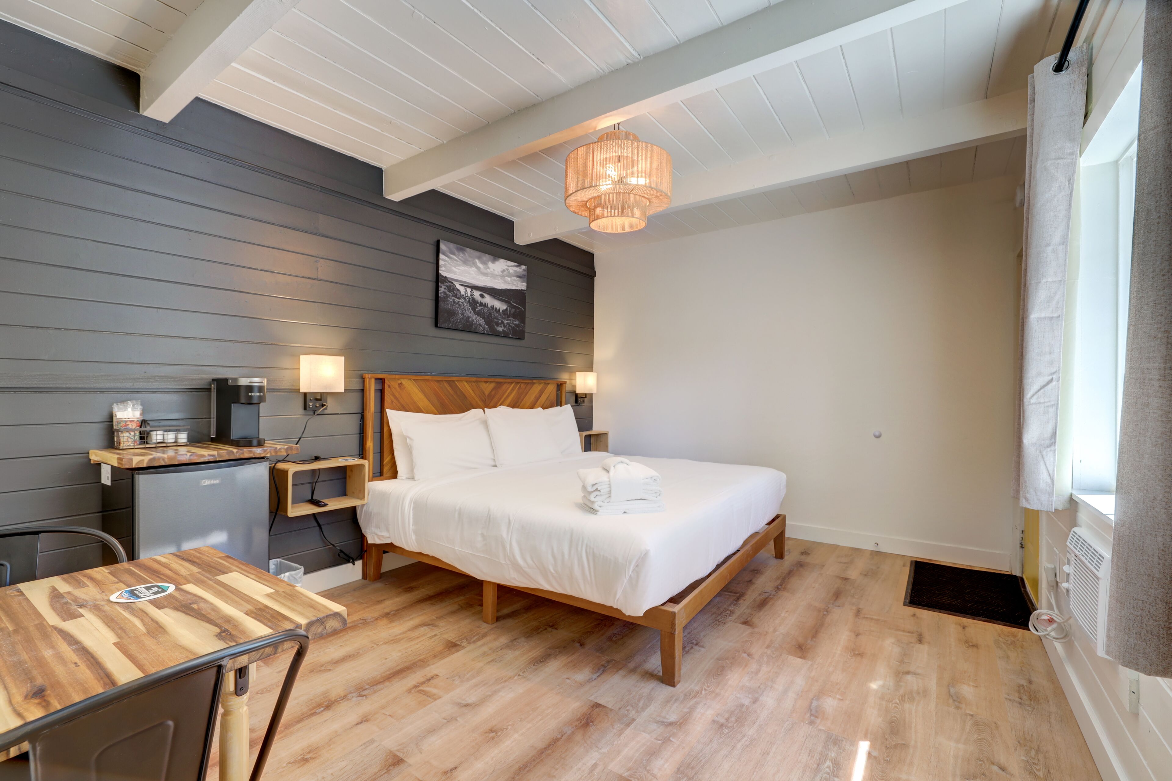 Et soveværelse med seng, natbord, lampe og et lille skrivebord med stol.