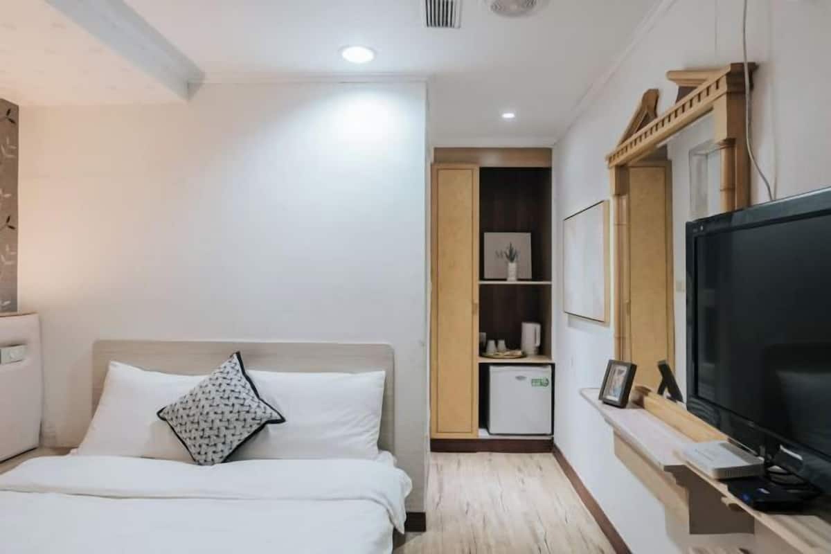 A hotel room with a bed, a TV, a small fridge, and a wooden cabinet.