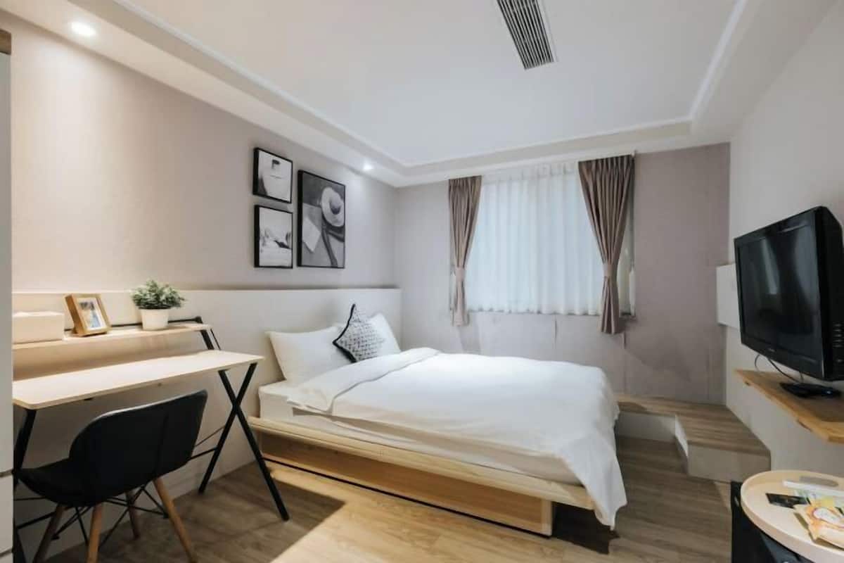 A modern bedroom with a bed, desk, chair, television, and artwork on the wall.