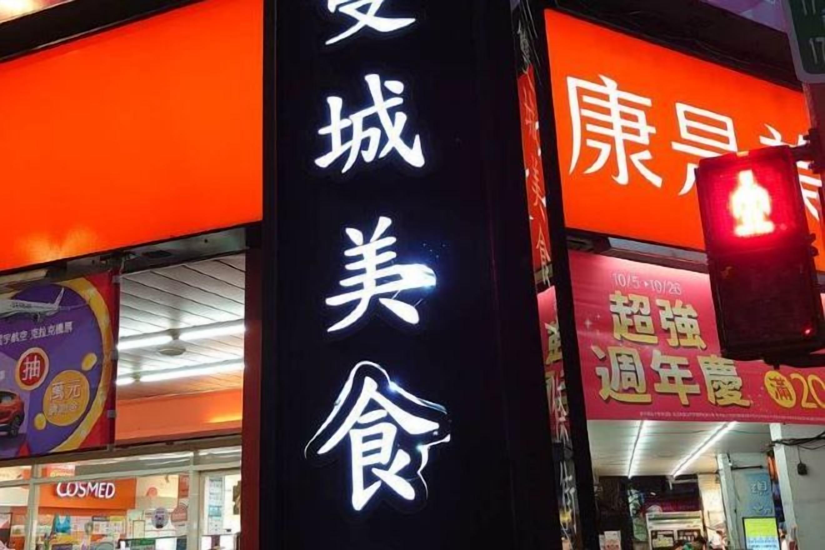 Une devanture de magasin avec un éclairage décoratif, comprenant une enseigne verticale bien visible avec du texte, ainsi qu’une enseigne horizontale avec du texte supplémentaire et une lumière rouge.