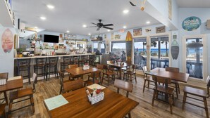 Un restaurant avec des tables et des chaises en bois, un coin bar et une vue sur la plage.