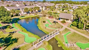 Un parcours de golf avec un étang, un pont et des bâtiments environnants.