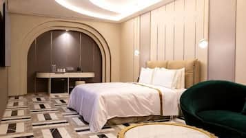 Una habitación de hotel con una cama, una mesa redonda, un sillón verde, un escritorio y un televisor.