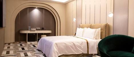 A hotel room with a bed, a round table, a green armchair, a desk, and a television.
