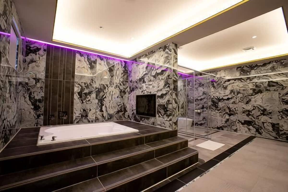 A modern bathroom with a large bathtub, marble walls, and a glass shower enclosure.