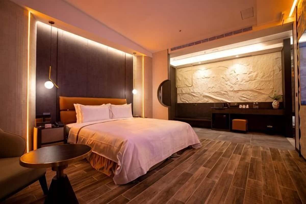 A hotel room with a large bed, a desk, a chair, and a TV.