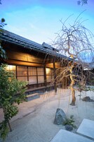 Un edificio japonés tradicional con tejado de tejas, paredes de madera y un camino de piedra que lleva a la entrada.