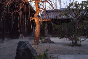 A traditional Japanese garden with a large rock, a tree with hanging branches, and a building in the background. - citrus house (Wakayama)